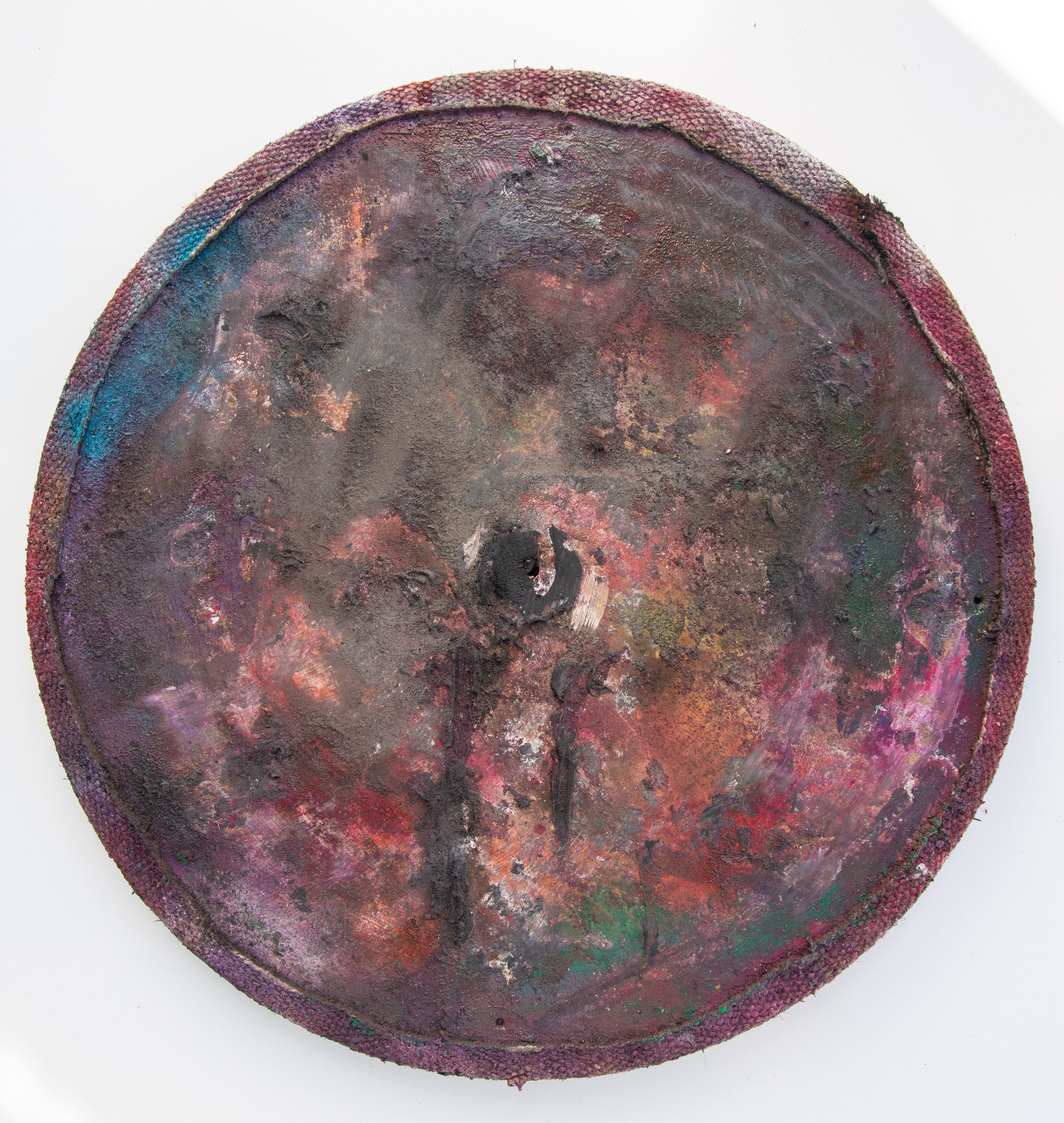 Round wood disc with a purple-magenta fabric binding at the rim. Inner surface in maroon, oxblood, and copper tones; pitted texture with a darker central core and a turquoise flare at upper left.